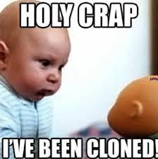 A baby with a shocked expression looks at another baby, or possibly a doll's head. Text above the image says "Holy crap" and below the image "I've been cloned!"