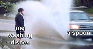 A man is standing in the street as a car drives through a puddle causing a big splash. Text overlay says "me washing dishes" on the left and "a spoon" on the right.