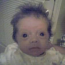 A baby with messy hair and a serious expression is looking straight at the camera.