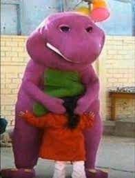 A person dressed as Barney the Dinosaur is hugging a child in front of a tan brick wall.