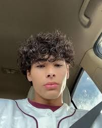 A young man with curly hair wearing a white baseball jersey.