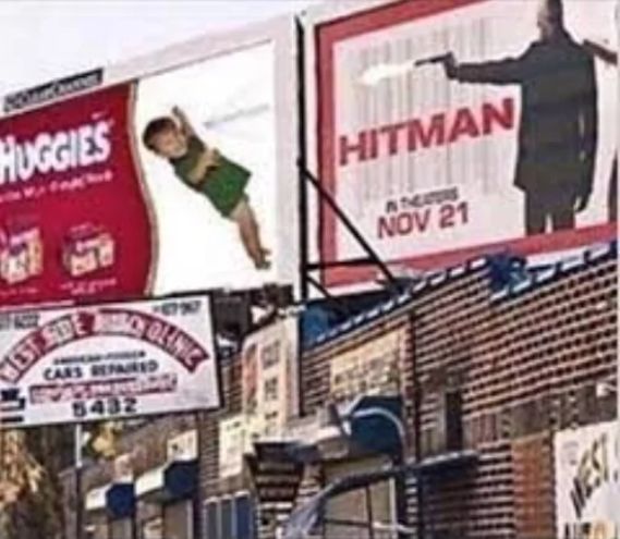 The image shows two adjacent billboards. The one on the left advertises "Huggies" diapers and features a baby swinging down. The billboard on the right advertises the movie "Hitman" with an image of a man pointing a gun. The text on the billboard says: "Hitman. In Theaters Nov 21." Below these two big billboards there is also a smaller billboard for "West Side Auto Clinic" that says: "Cars Repaired".