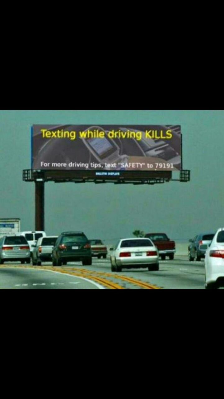 A billboard on a highway with multiple cars in the foreground. The billboard reads: "Texting while driving KILLS. For more driving tips, text "SAFETY" to 79191."