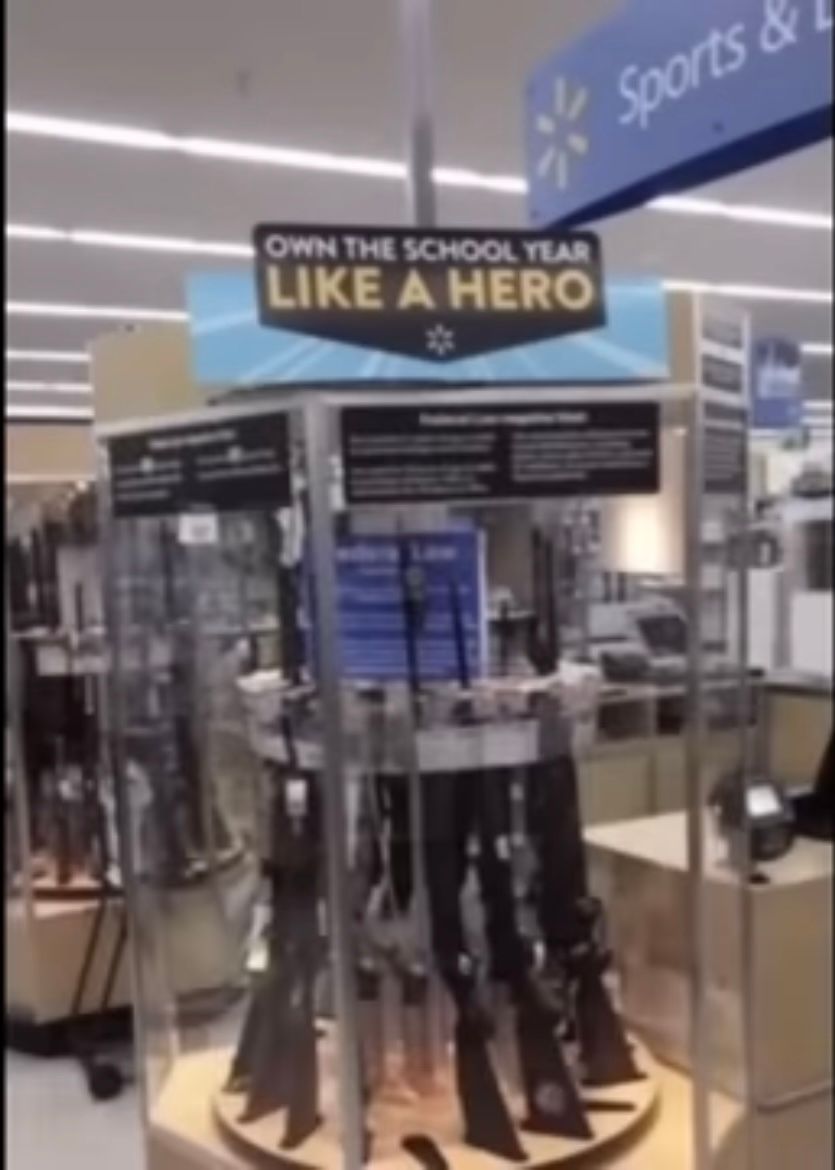 A display of rifles in a retail store with a sign above it that reads "OWN THE SCHOOL YEAR LIKE A HERO".