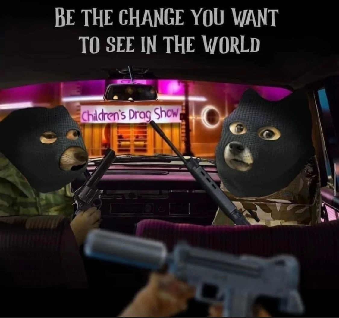 Two dog characters wearing ski masks, armed with weapons, sitting in a car. In the background, a sign is visible that reads "Children's Drag Show". Above the dogs, the text says "BE THE CHANGE YOU WANT TO SEE IN THE WORLD".