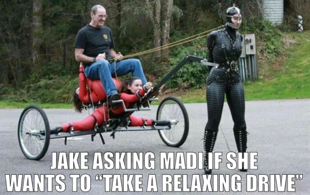 A man is sitting on a contraption with wheels. The woman in the red suit is attached to it. Another woman with a black leather outfit and a mask is pulling the contraption with a rope. Text on the image says "Jake asking Madi if she wants to "take a relaxing drive"."