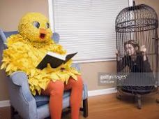 A person in a large yellow chicken costume is sitting in a blue chair, reading a book. To the right, a person is in a birdcage. The caption states "The reason we will never have reparations for slavery."