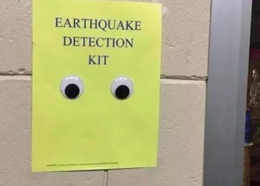 A yellow piece of paper attached to a wall reads "EARTHQUAKE DETECTION KIT". Two googly eyes are attached to the paper below the text.