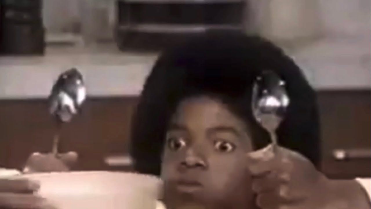 A still from the movie "Captain Eo" showing Michael Jackson looking to either side where two spoons are pointing at him. The text reads: Me at the dinner table.