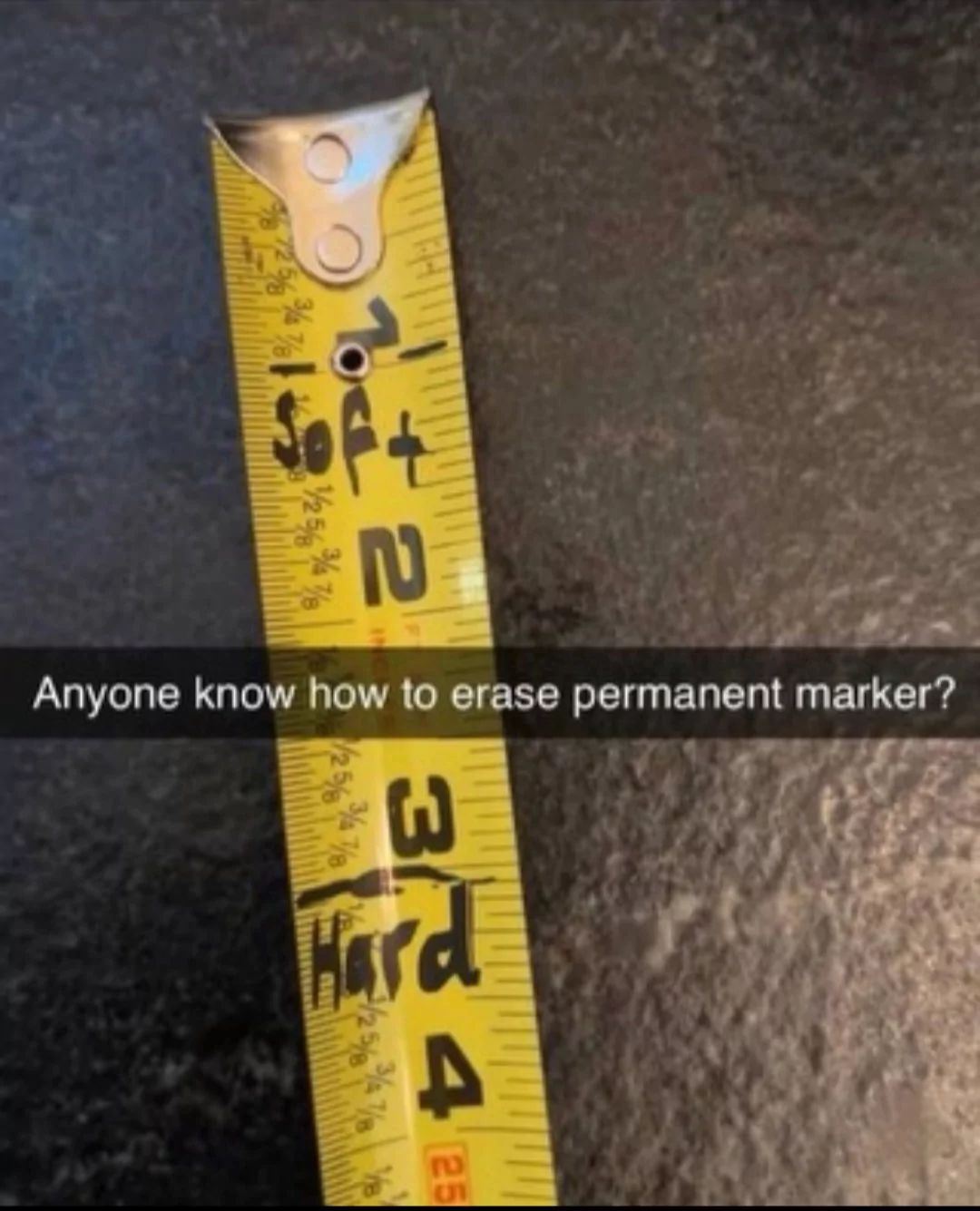 A close-up shot of a yellow tape measure on a dark surface. The text "1ft" and "3ft" are visible. The tape measure has the words "1ft" and "3ft" written with a permanent marker. Below the tape measure there is the text: "Anyone know how to erase permanent marker?"